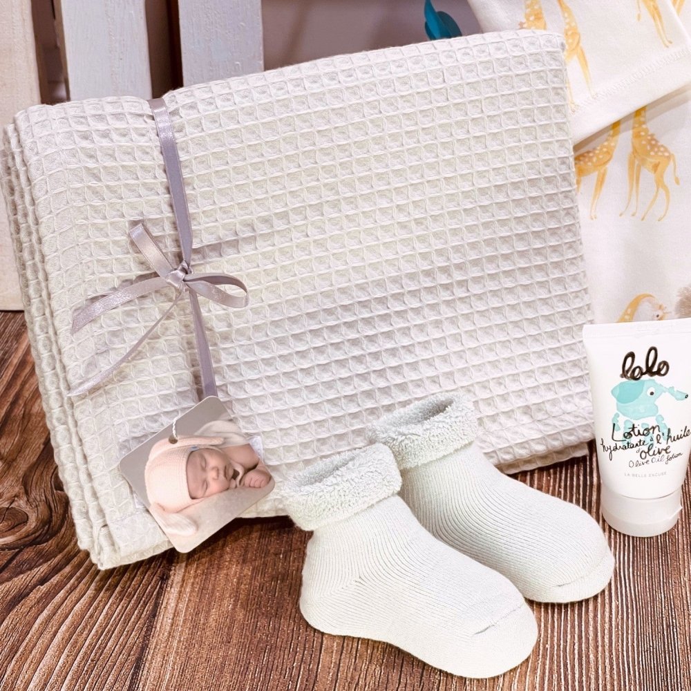Baby gift set with elephant-print onesie, grey waffle blanket, plush giraffe rattle, terry booties, and Quebec-made baby lotion.