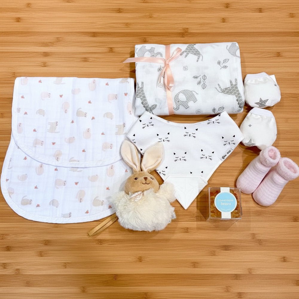 baby girl gift with swaddle blanket, burp pad, bib with silicone teether, socks, scratch mittens, Sugarfina champagne gummie bears.