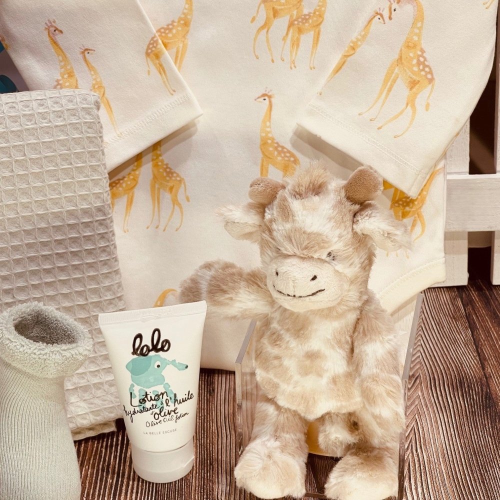 Baby gift set with elephant-print onesie, grey waffle blanket, plush giraffe rattle, terry booties, and Quebec-made baby lotion.